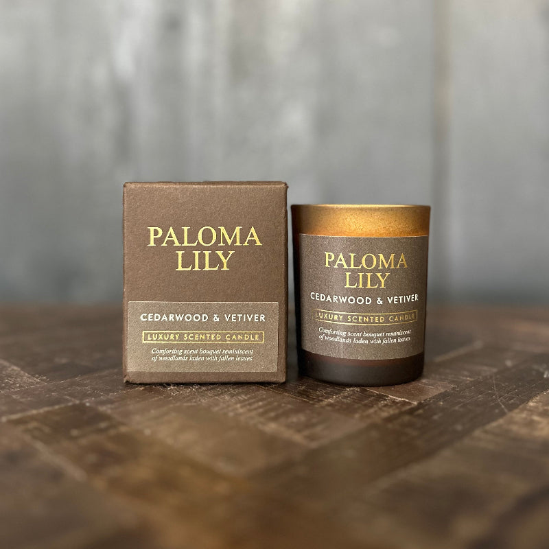 Paloma Lily candle and packaging on a wooden surface with a blurred background