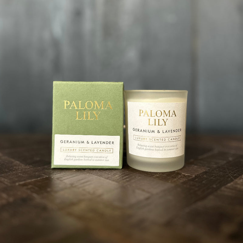 Paloma Lily geranium and lavender candle and packaging on a wooden surface with a blurred background