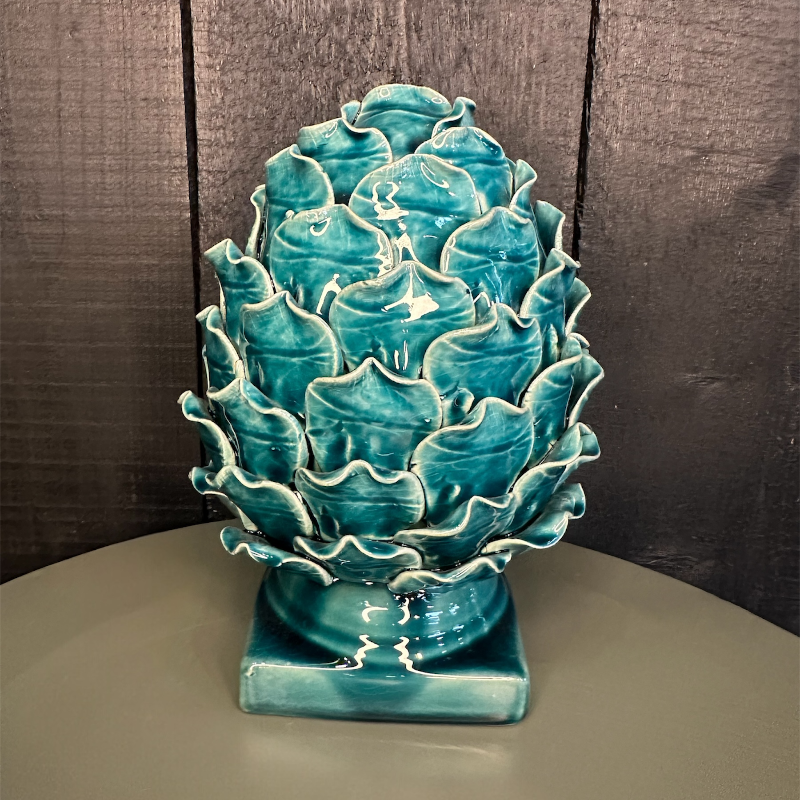 Turquoise ceramic artichoke sculpture on a neutral surface with a dark wooden background